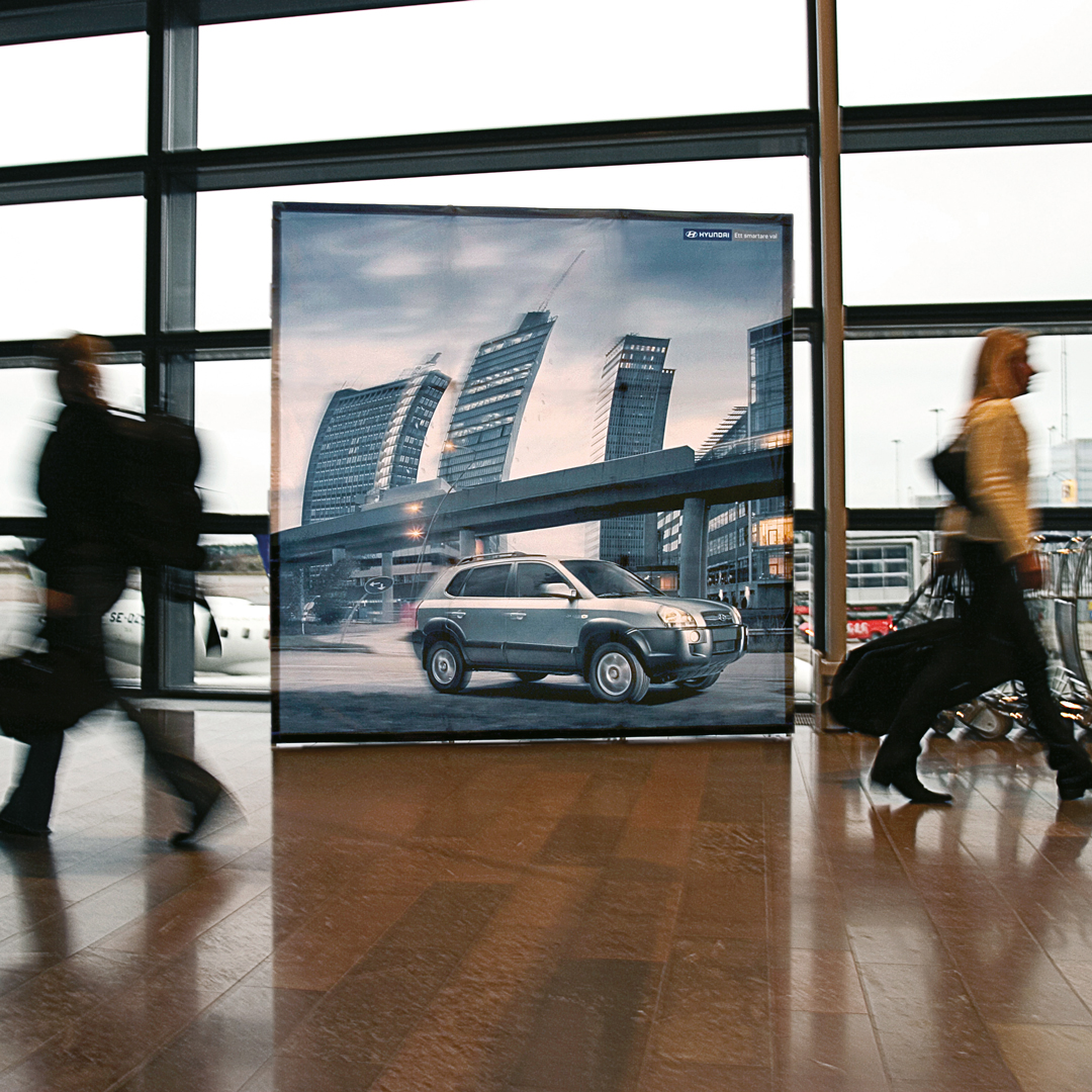 Messewand Domo ohne Seitenklappen mi bedruckter Bespannung steht in einer offenen Halle mit vorbeigehenden Personen.